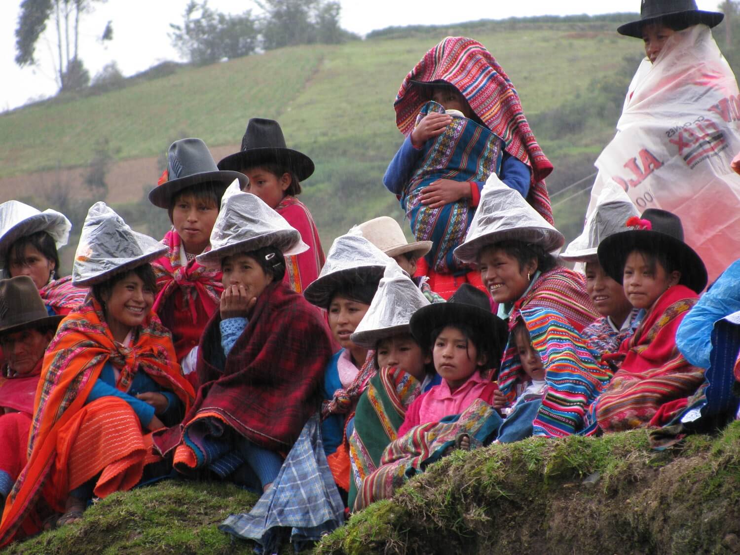 Local women and children protect themselves from the rain by putting a plastic bag on their hats and colorful ponchos around their shoulders. Community-based tourism in Peru - RESPONSible Travel Peru