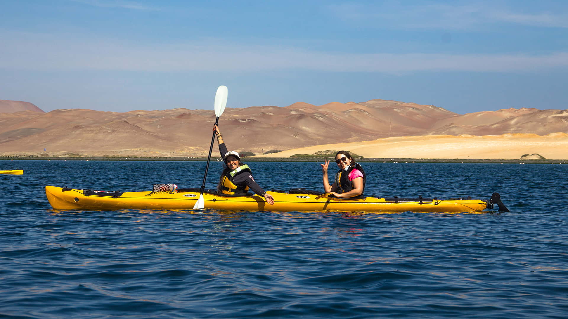Two girls in the same kayak saluting the camera | Responsible Travel Peru