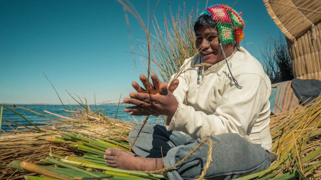 Man sitting on island floor while using hands and feet when making totora strands | Responsible Travel Peru