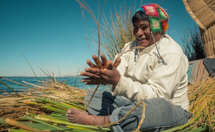 Man sitting on island floor while using hands and feet when making totora strands | Responsible Travel Peru