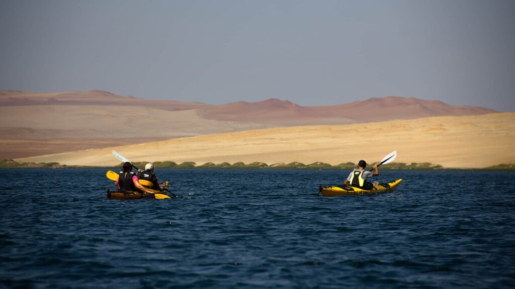 two kayaks cruising over deep blue waters and montanous desert in the back | Responsible Travel Peru