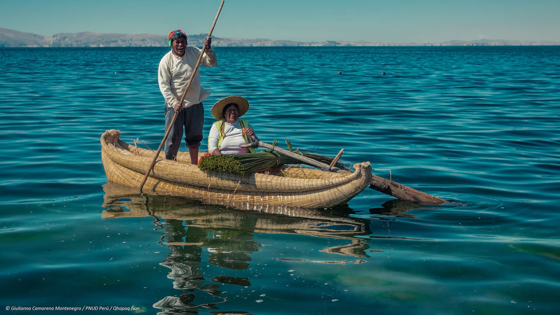 Man (paddeling) and woman (sitting) on a reed boat while navigating over the water | Responsible Travel Peru