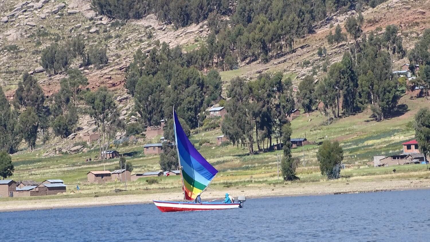 Sailboat with a sail in the colors of the Inca flag sailing by the shores of Capachica | RESPONSible Travel Peru