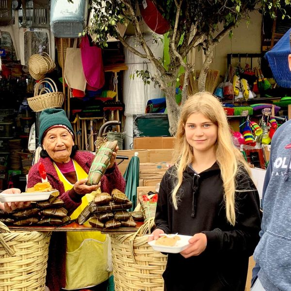 Father and sons (boy and girl) buy tamales to an old vendor lady in the street | Impactful Travel Peru