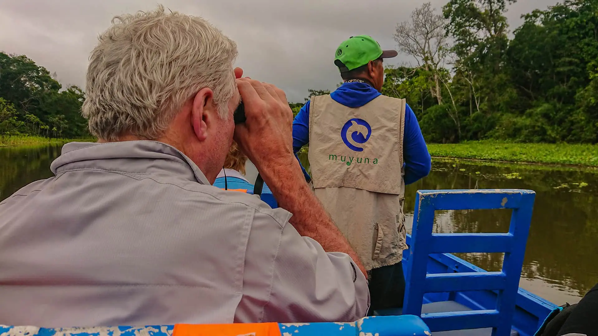 Man with binoculars behind guide on a river boat | Responsible Travel Peru