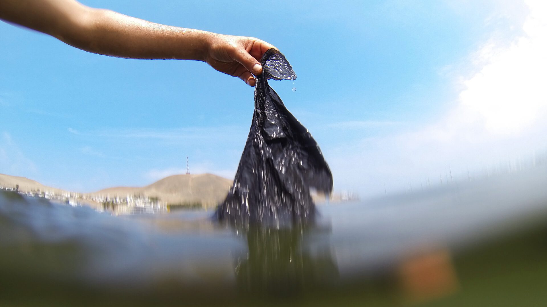 A person removing a black plastic bag from the sea | RESPONSible Travel Peru