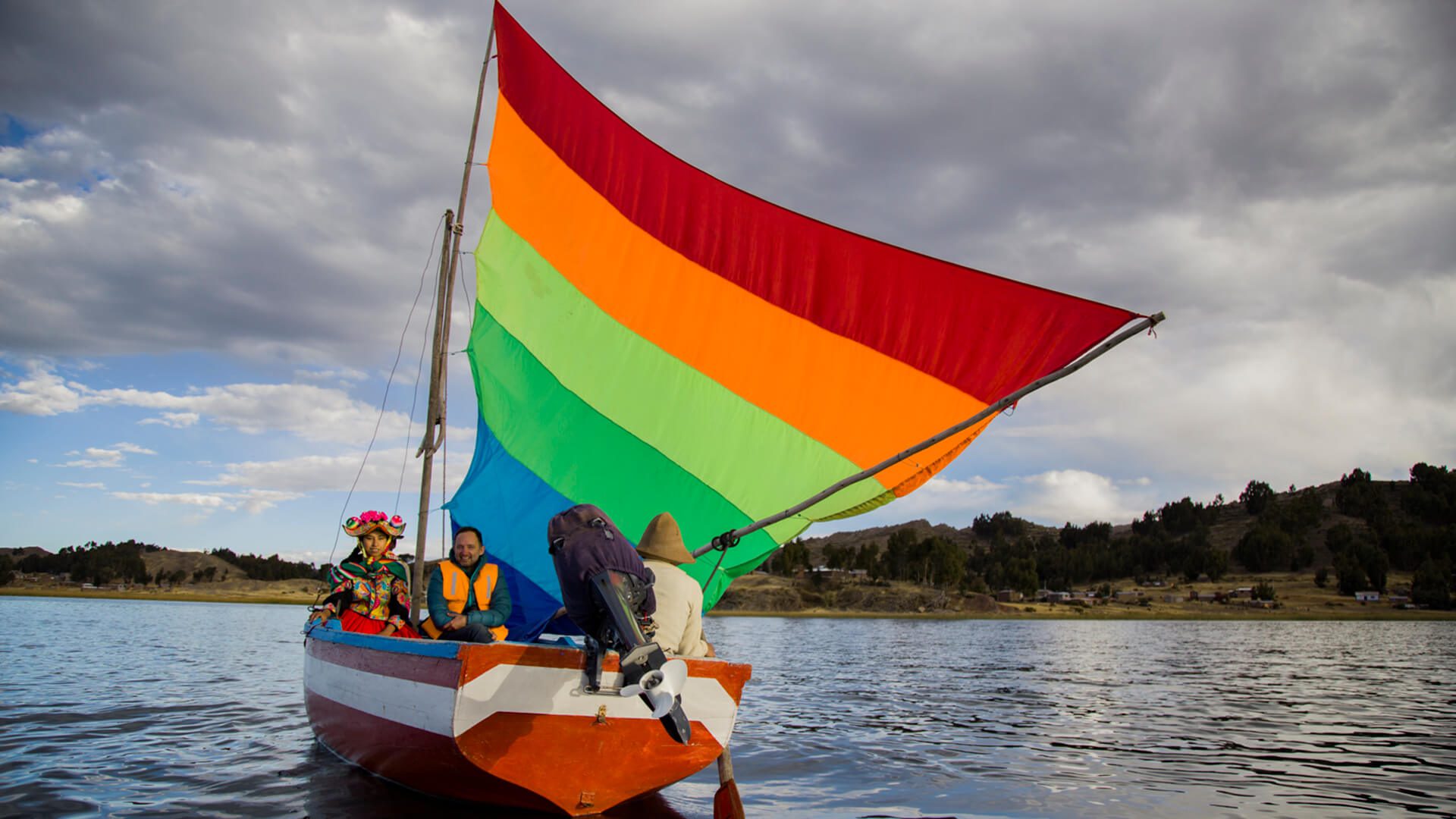 A rainbow-sailed boat carrying a passenger a young local lady in traditional costume in Titicaca lake | RESPONSible Travel Peru