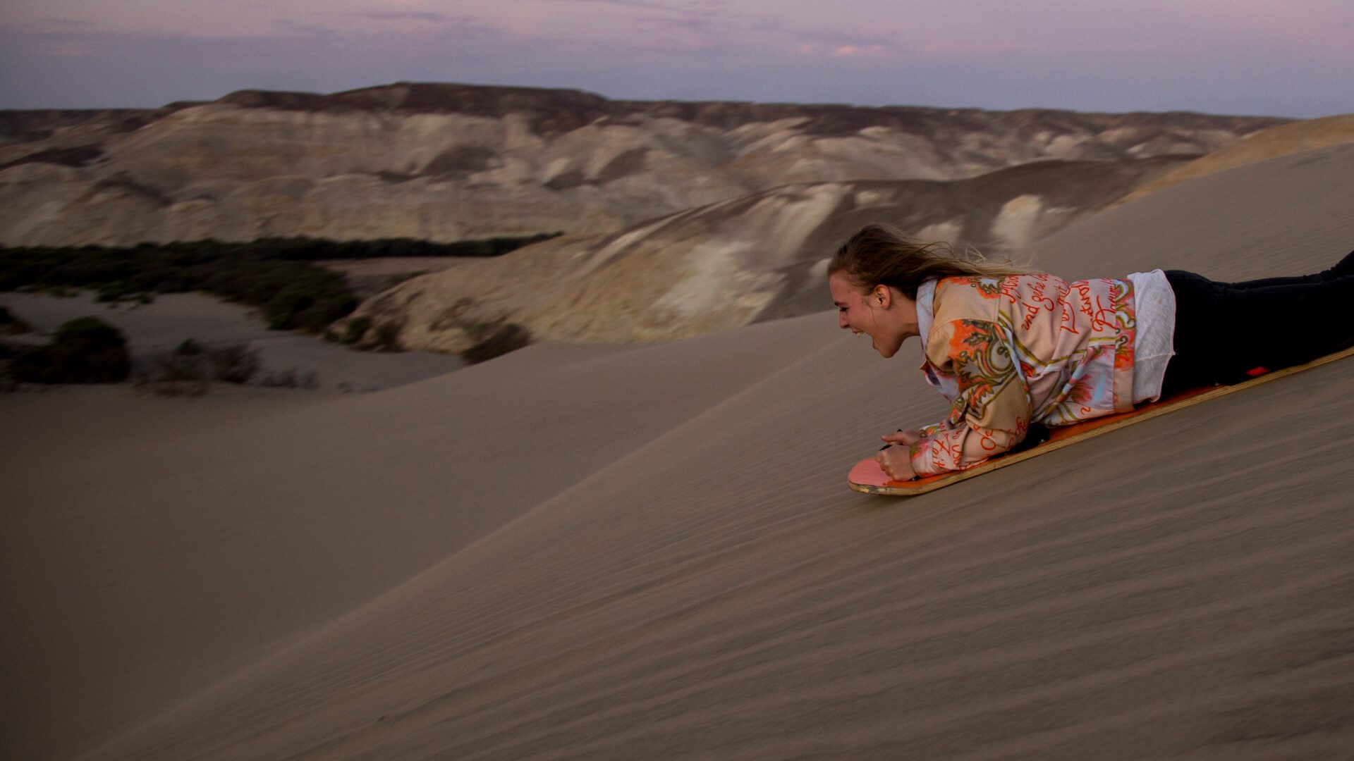 Girl sandboarding down a dune in the Nazca desert | RESPONSible Travel Peru