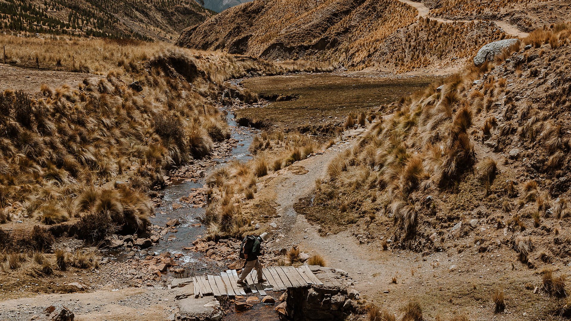 Man crossing small bridge over ravine in Andes grassland | RESPONSible Travel Peru | Photo by Bjorn Snelders