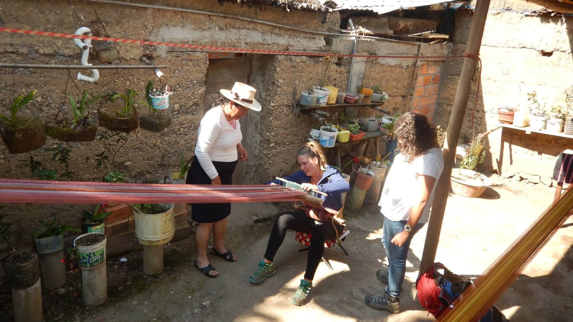 Two local women guiding a young foreigner lady in the use of the traditional loom