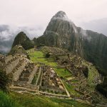 Aerial view of Machu Picchu ruins with stone structures and terraces, surrounded by lush green mountains and mist. Aerial view of Machu Picchu ruins with stone structures and terraces, surrounded by lush green mountains and mist.