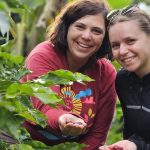 Two people smiling and holding berries in their palms, surrounded by green foliage.