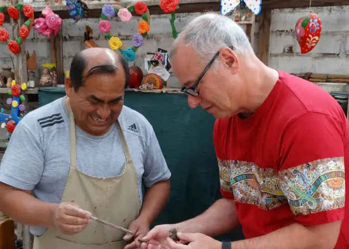 Two men crafting pottery together in a workshop, surrounded by colorful decorations and tools.