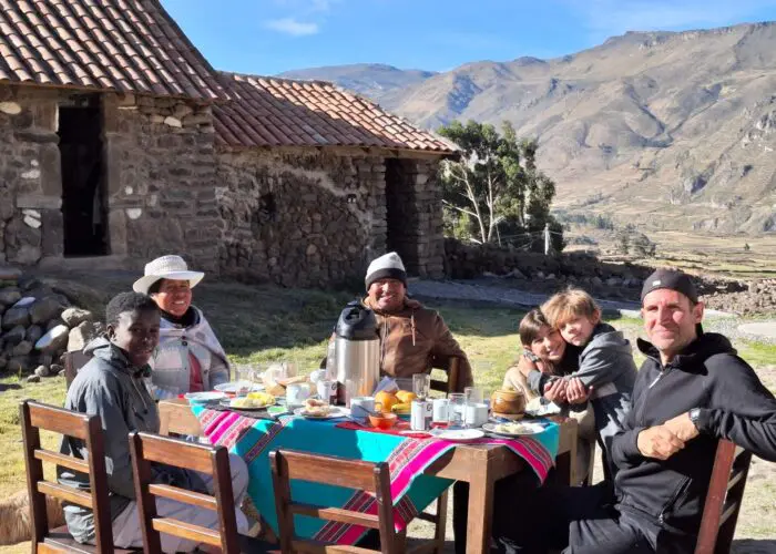 A German family enjoys breakfast in the sun in Coporaque homestay (tiny), with mountains and the stone building of their Coporaque homestay in the background. | Impactful Travel Peru
