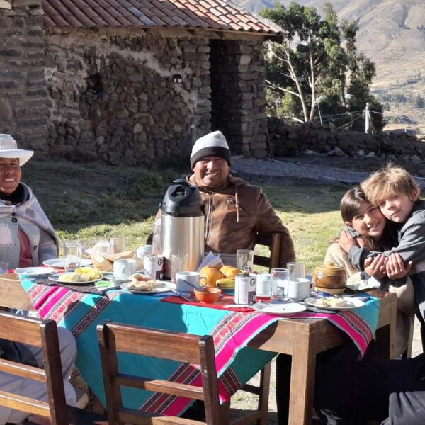 Six people enjoy a meal outdoors with Impactful Travel, highlighting authentic, community-based tourism by a stone building and mountains.